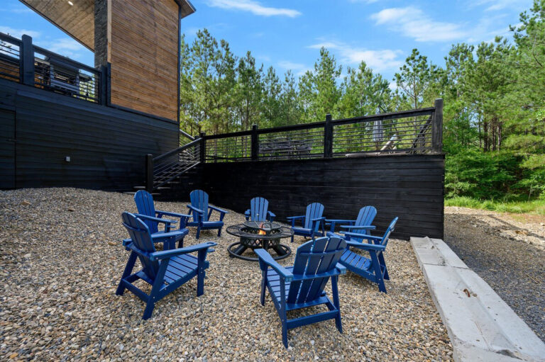 Circle of Adirondack chairs surrounding a stone firepit with a backdrop of trees at the Aquarius cabin.