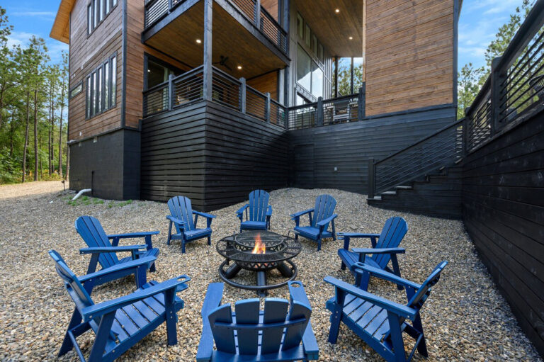 Outdoor firepit surrounded by Adirondack chairs on a stone patio, nestled among trees at the Aquarius cabin.