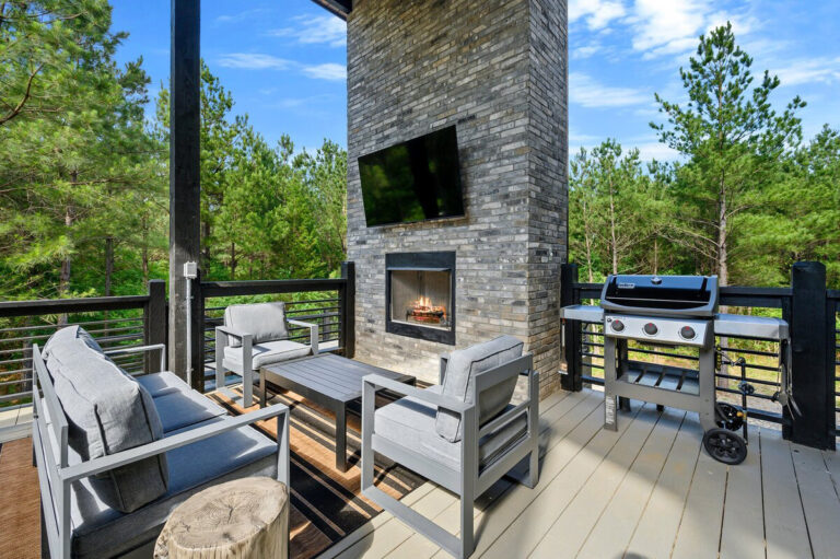 Spacious outdoor deck featuring a cozy sitting area, stone fireplace, and built-in grill at the Aquarius cabin.