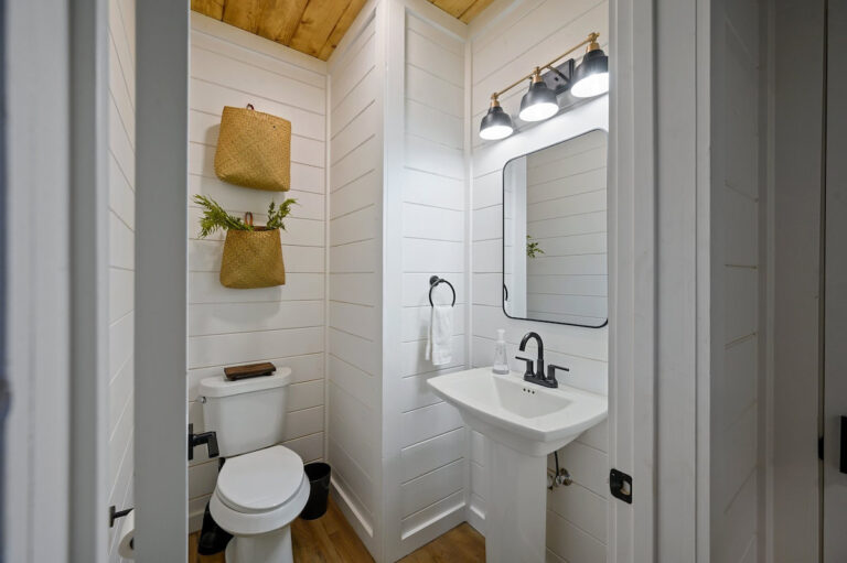 Bathroom with a white pedestal sink, white paneled walls, and a warm wood ceiling.