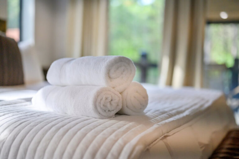 Neatly rolled white towels placed at the foot of a neatly made bed in a cozy cabin bedroom.