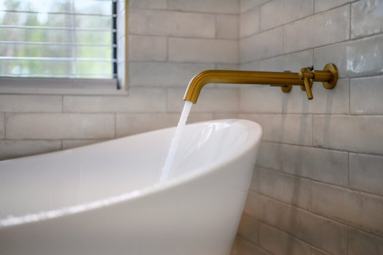 Close-up of a white soaking tub with polished brass faucet and handles.