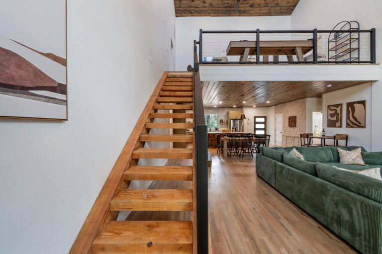View from stairway overlooking the open-concept living room and kitchen with wood accents and high ceilings.