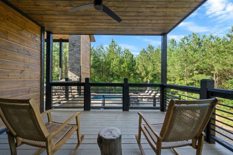 Balcony sitting area with rocking chairs and a small table, overlooking the surrounding forest.