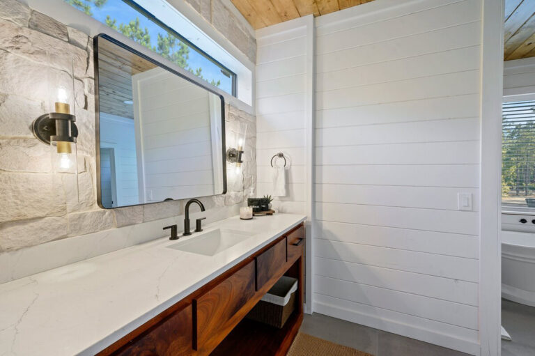 Bathroom sink with modern faucet, large framed mirror, and a window positioned above the mirror letting in natural light.