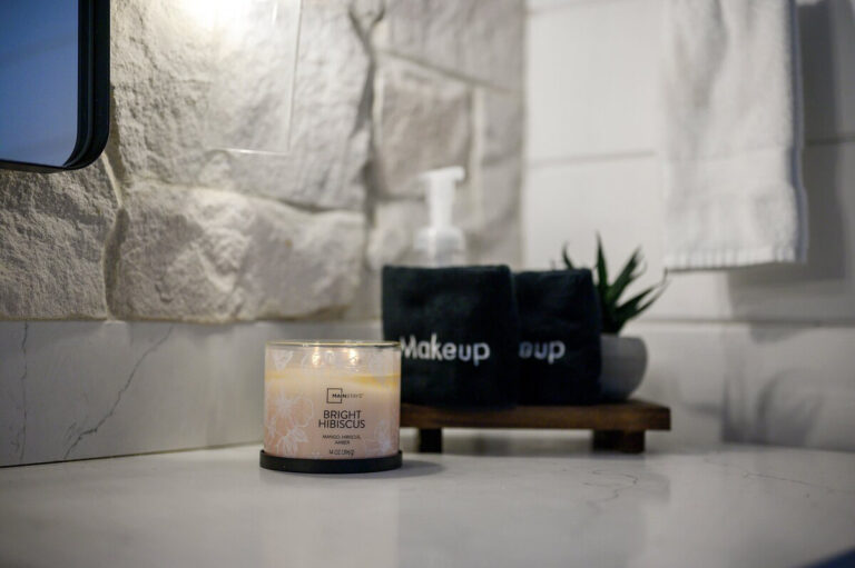 Close-up of a lit candle, small green plant, and neatly arranged bathroom amenities on a countertop.