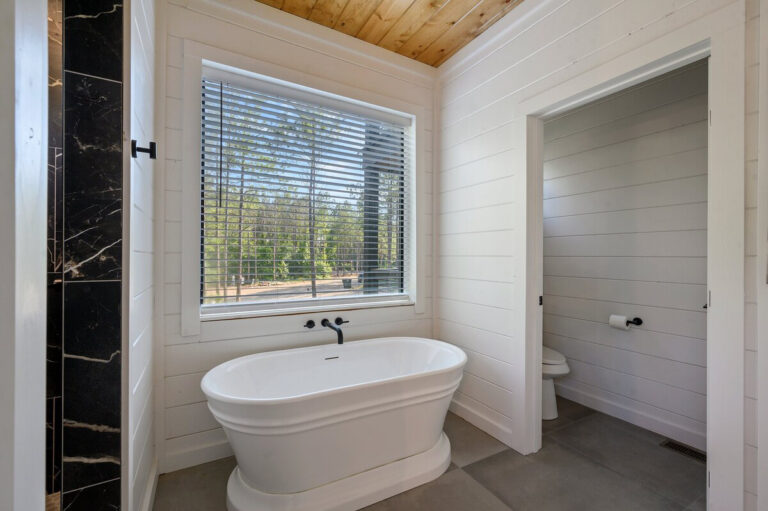 Soaking tub corner view with black fixtures and large window showing forest scenery.