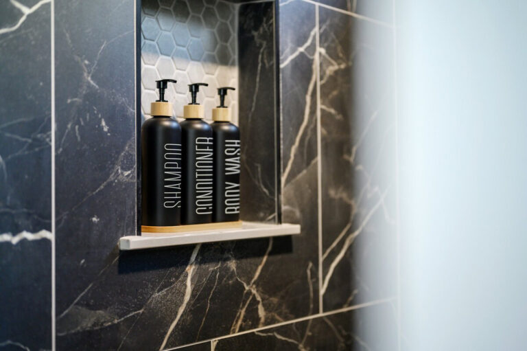 Built-in shower shelf stocked with shampoo, conditioner, and body wash bottles in a tiled shower.