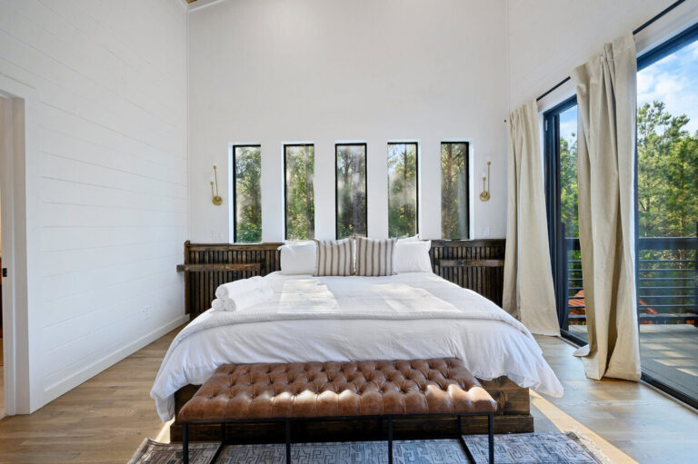 Spacious bedroom with white bedding, large picture windows, and sliding glass doors opening to the outdoors.