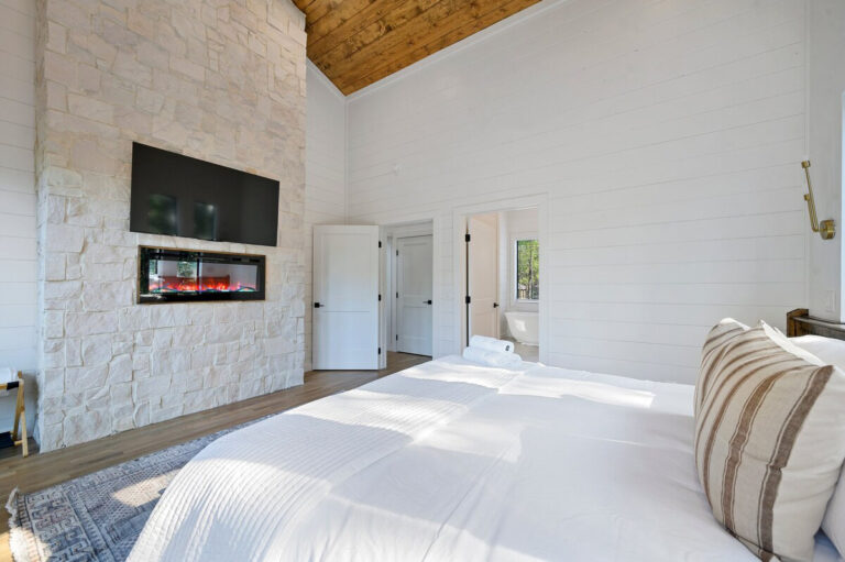 Stylish bedroom with fresh white bedding and a sleek built-in fireplace set into the wall.
