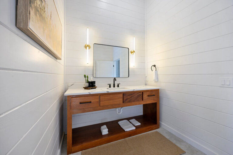 Alternate view of a bathroom with wood cabinetry, white surfaces, paneled walls, and a gold-framed mirror.