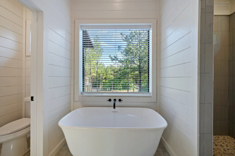 Large soaking tub beneath a wide picture window, featuring modern black fixtures and natural light.