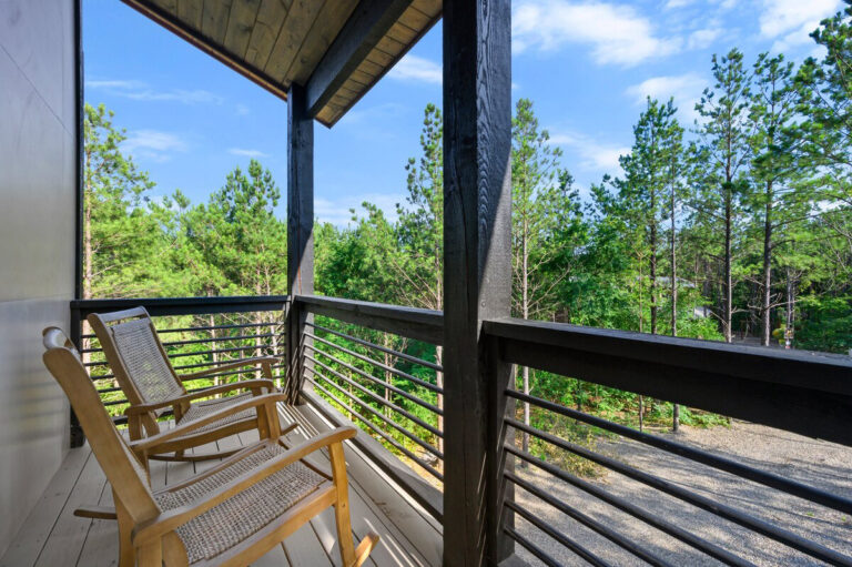 Two wooden rocking chairs on the balcony facing outward, overlooking the peaceful forest landscape.