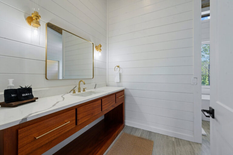 Bathroom with wood vanity, white countertop, white paneled walls, and a large mirror with a gold frame.