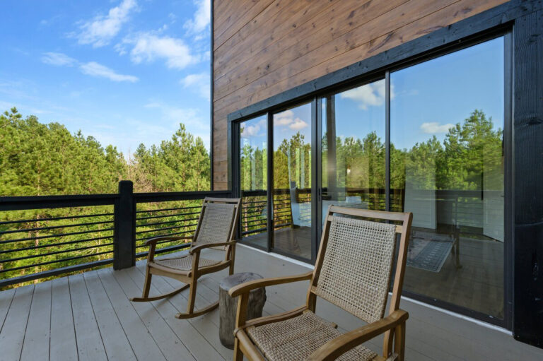 Wooden rocking chairs on the balcony with the cabin’s large picture windows reflecting the outdoor surroundings.