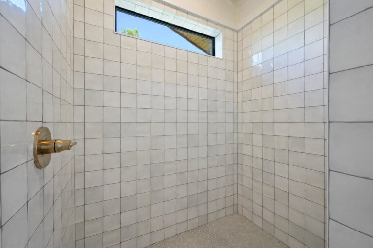 Spacious shower with white tile, a large window for natural light, and brass fixtures.