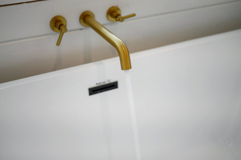 Close-up of polished brass bathtub faucet and handles set against a white surface.