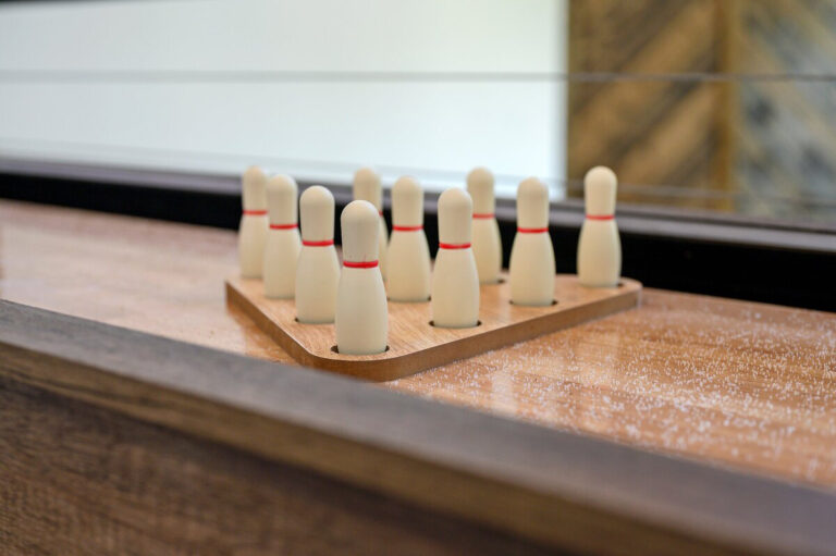 Close-up of a shuffleboard table featuring miniature bowling pins set up for a tabletop bowling game.