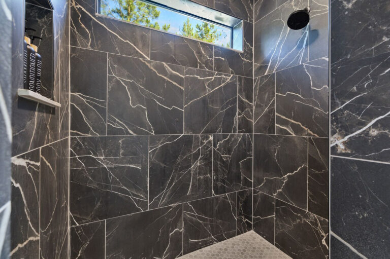Spacious walk-in shower featuring black and gold marble tile and windows that allow natural light to filter in.