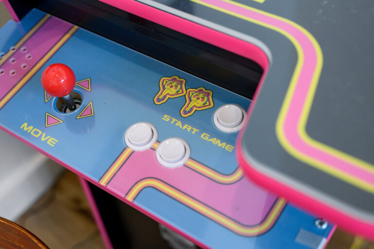Close-up of the Pac-Man arcade machine showing the joystick, colorful buttons, and retro screen graphics.