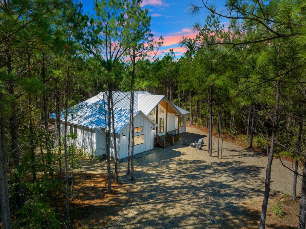 Exterior view of the splish splash cabin by mountain fork vacations, featuring a modern design with large windows, surrounded by tall pine trees in hochatown, oklahoma.