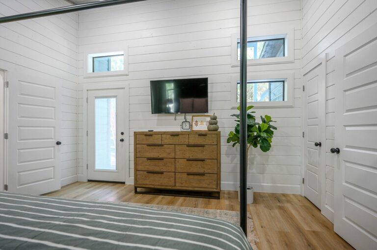 Modern rustic bedroom with tall ceilings, wood dresser, and flat-screen TV for a couple's getaway