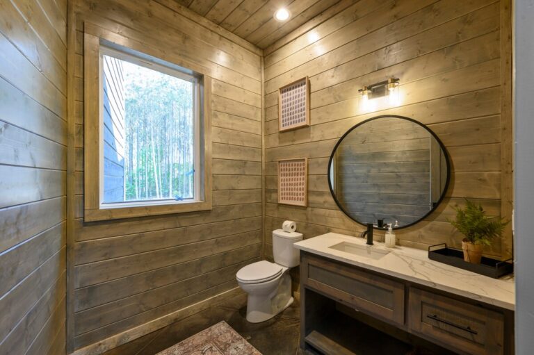 Rustic bathroom with wood panel walls and round mirror perfect for family reunion