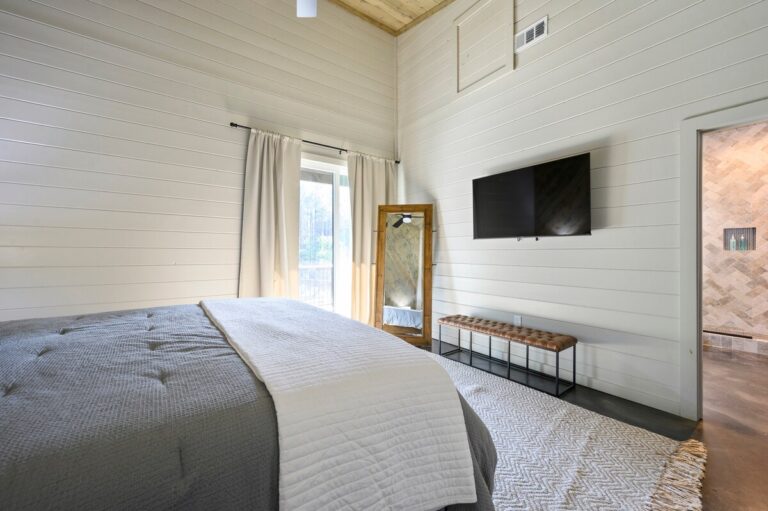 Bedroom with gray bedding, wall-mounted TV, and full-length mirror