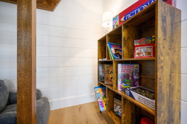 Family game shelf inside Blue Note Broken Bow cabin with board games and cozy seating near outdoor fire pit and river activities.