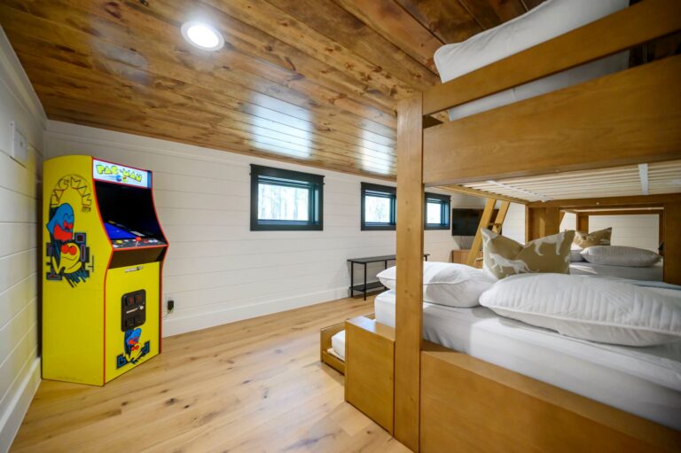 Bunk room with arcade game inside Blue Note Broken Bow cabin designed for family fun near outdoor fire pit and river activities.