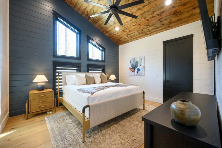 Modern luxury bedroom inside Blue Note Broken Bow cabin with vaulted wood ceilings and cozy furnishings near outdoor fire pit and river activities.