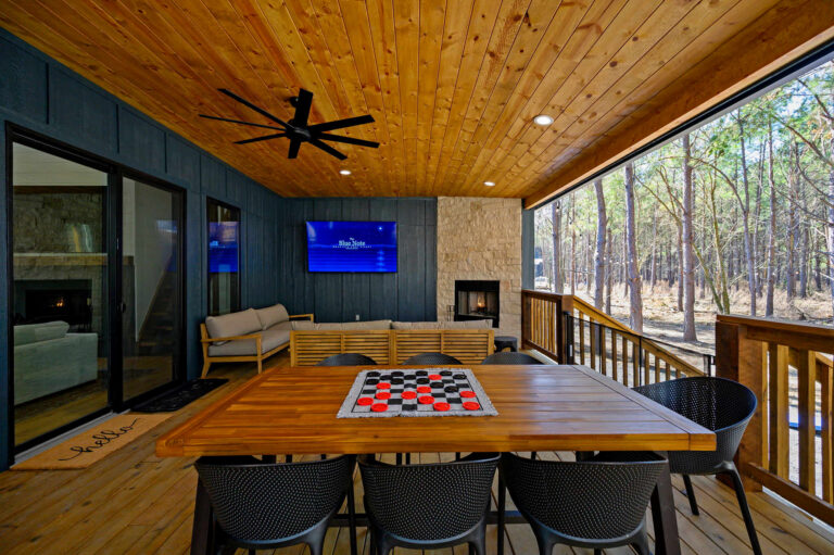 Covered patio gathering area at Blue Note Broken Bow cabin with dining table, fireplace, TV, and outdoor entertainment amenities.