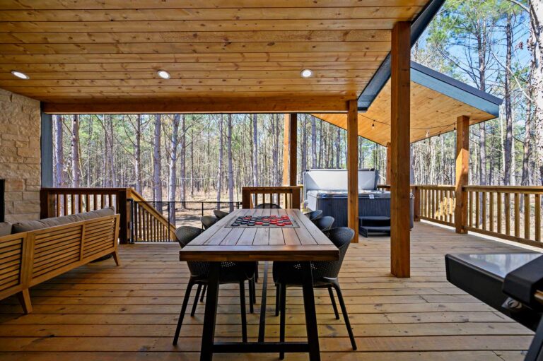 Spacious outdoor dining patio at Blue Note Broken Bow cabin with hot tub, covered seating, and forest views.