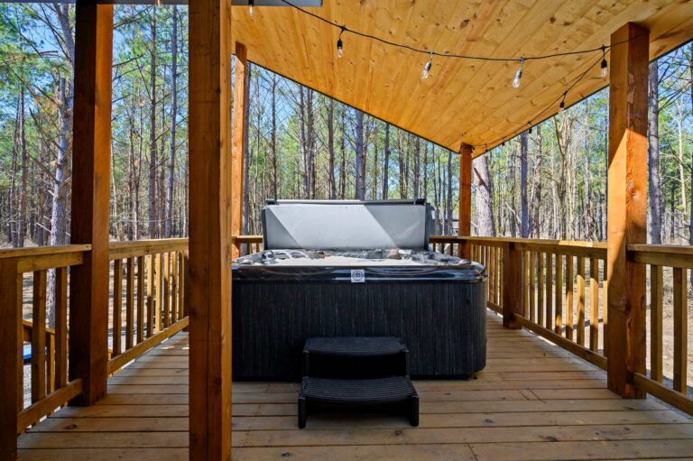 Covered deck hot tub at Blue Note Broken Bow cabin surrounded by wooded scenery and luxury outdoor amenities.