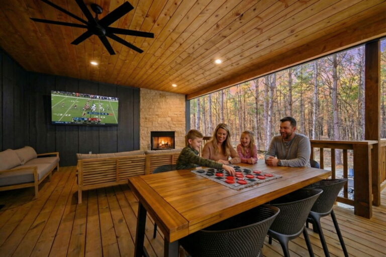 Covered outdoor living and dining area at Blue Note Broken Bow cabin with fireplace, TV, and family gathering space.
