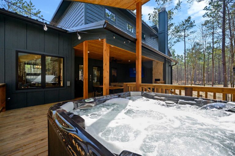 Luxury hot tub on covered deck at Blue Note Broken Bow cabin surrounded by forest views and outdoor entertainment space.