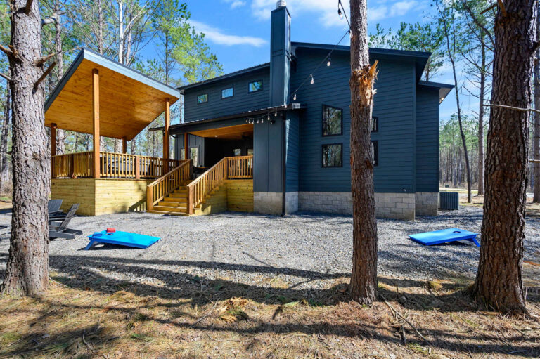 Daytime exterior of Blue Note Broken Bow luxury cabin with covered patio, forest surroundings, and outdoor recreation space.