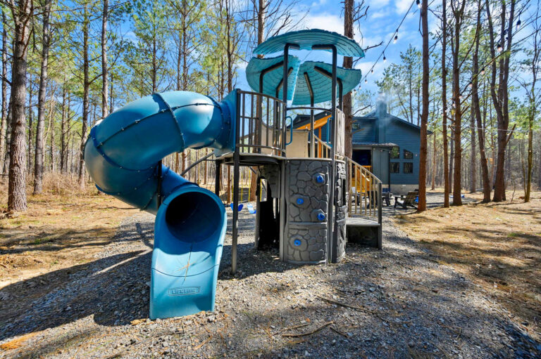 Large outdoor playground slide and play structure at Blue Note Broken Bow cabin surrounded by pine trees and family-friendly amenities.